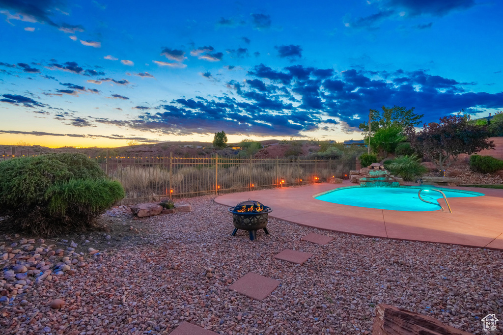 Pool at dusk with fence, a fenced in pool, a fire pit, and a patio