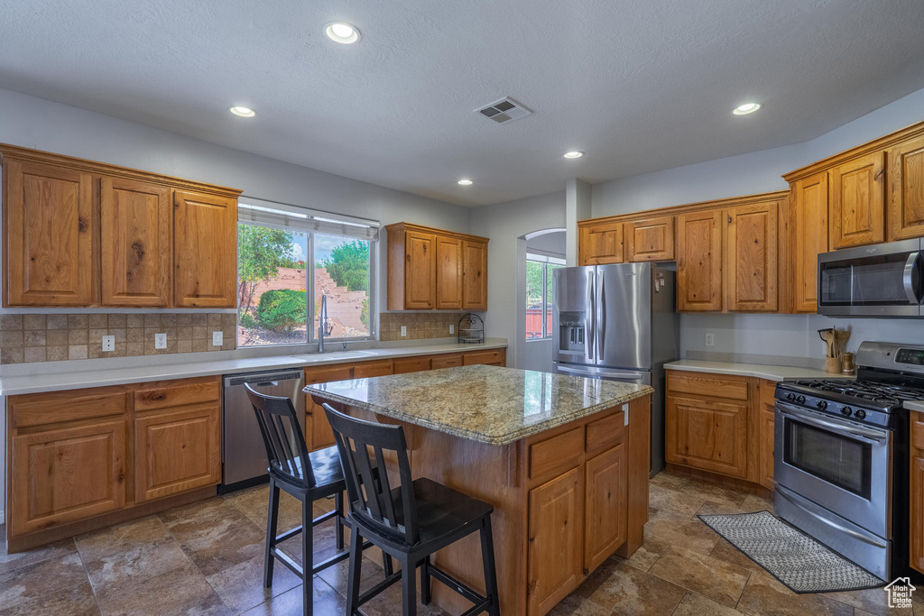 Kitchen with appliances with stainless steel finishes, a sink, backsplash, a kitchen island, and visible vents