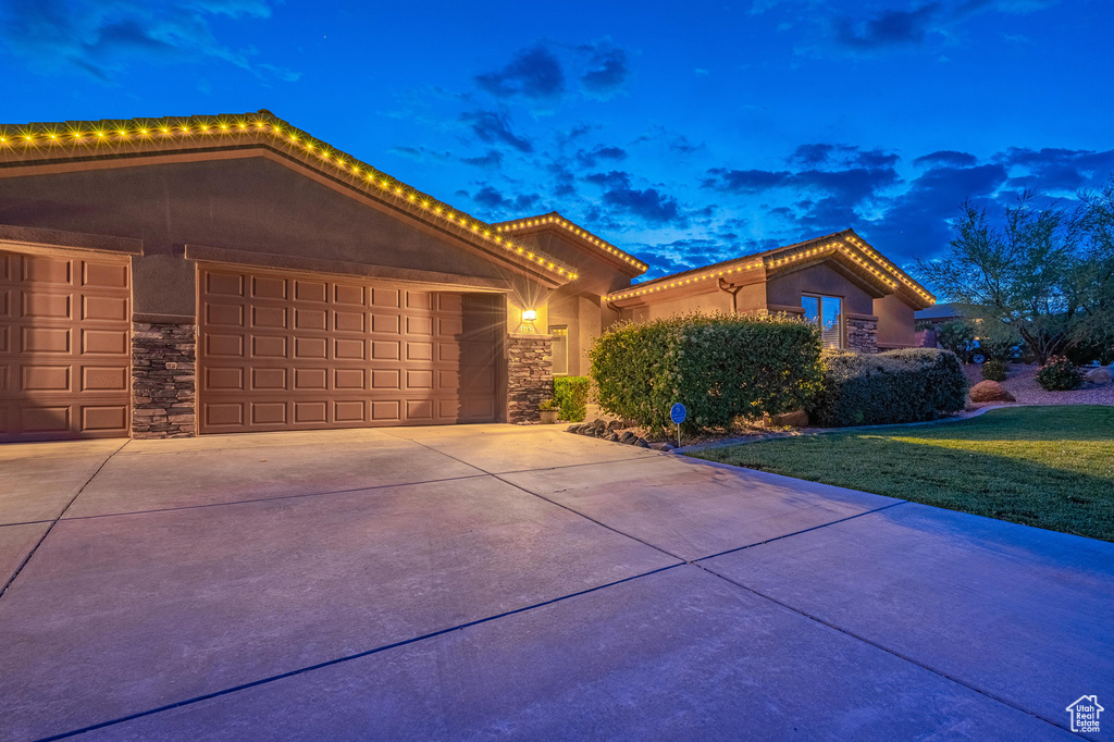 View of front facade with an attached garage, stucco siding, driveway, and stone siding
