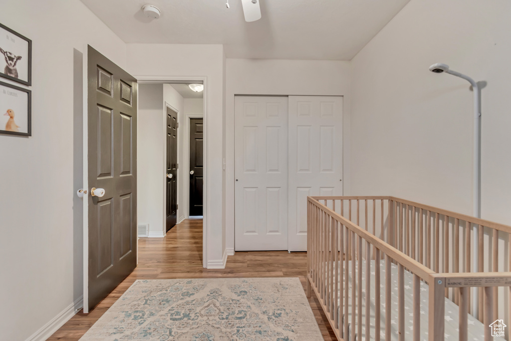 Unfurnished bedroom featuring a nursery area, light wood-type flooring, ceiling fan, and a closet