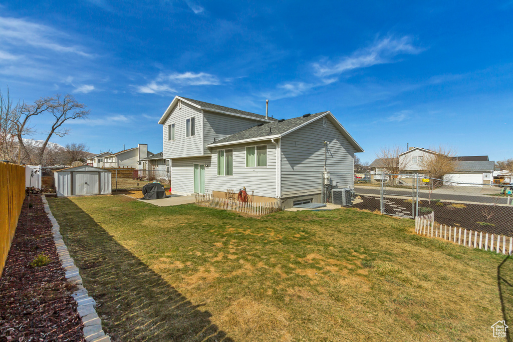 Rear view of property featuring an outbuilding, cooling unit, a yard, a fenced backyard, and a storage unit