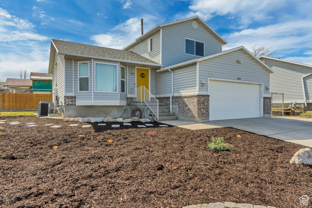 Tri-level home featuring central air condition unit, driveway, a garage, and fence