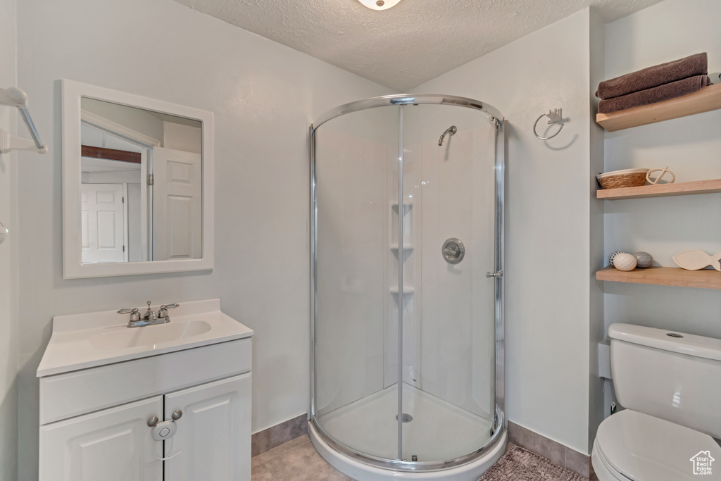 Bathroom featuring tile patterned flooring, an enclosed shower, vanity, a textured ceiling, and toilet