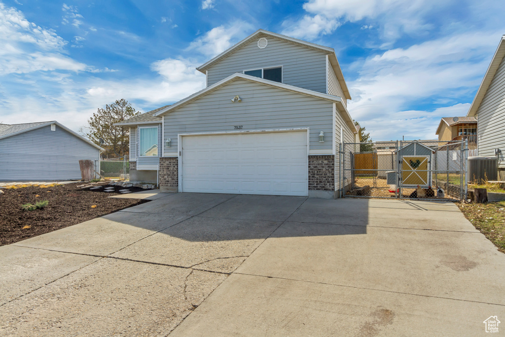 View of side of property featuring a garage, concrete driveway, a gate, and brick siding