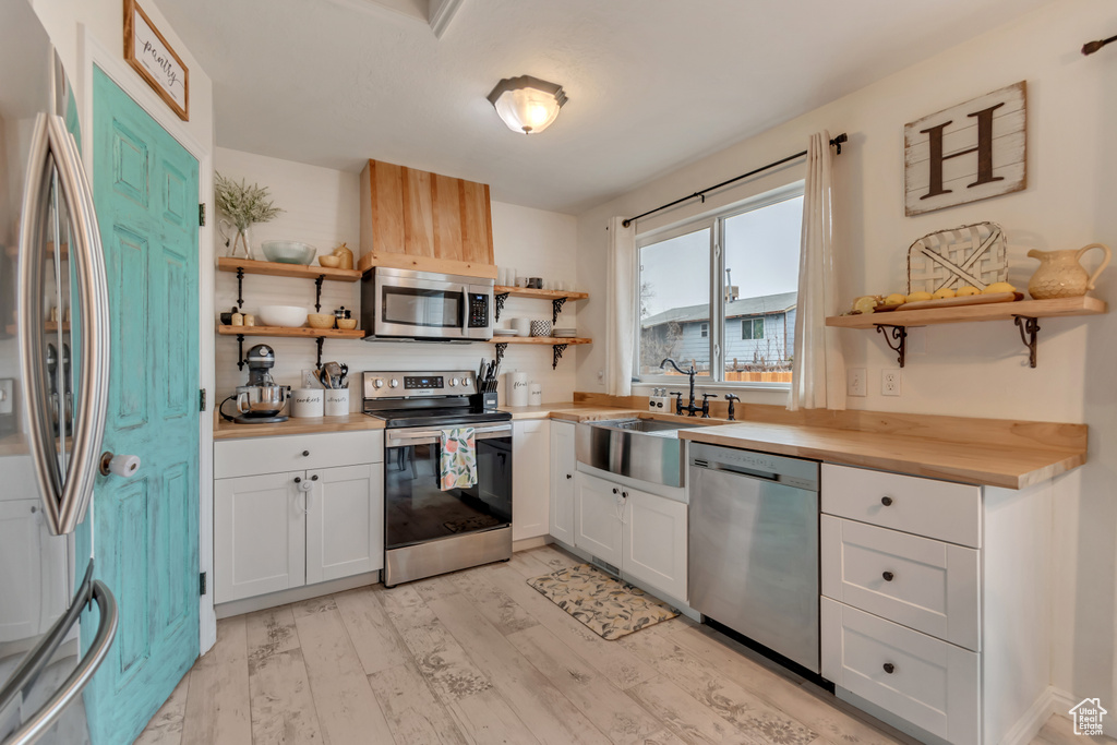 Kitchen with butcher block counters, sink, white cabinetry, light wood-type flooring, and appliances with stainless steel finishes