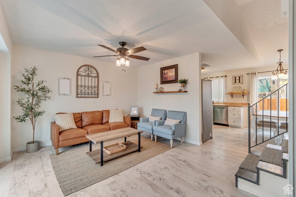 Living room featuring ceiling fan with notable chandelier and light hardwood / wood-style flooring