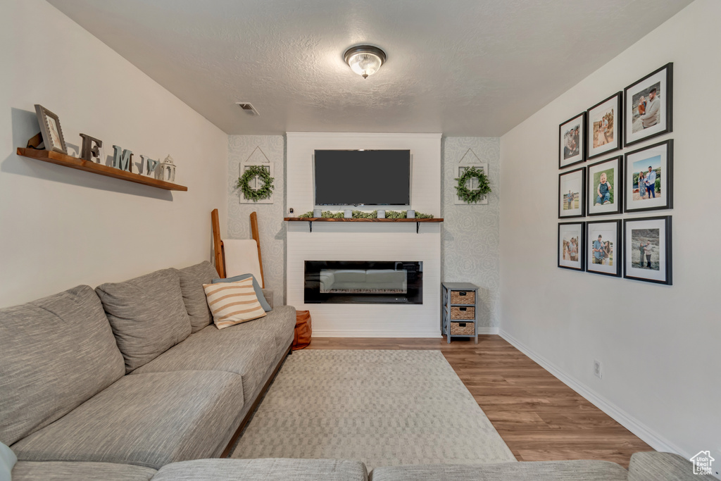 Living room featuring wood-type flooring, a large fireplace, and a textured ceiling