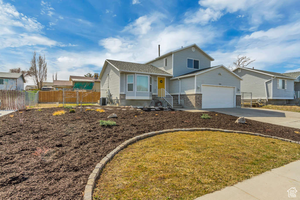 Split level home with an attached garage, fence, brick siding, and driveway