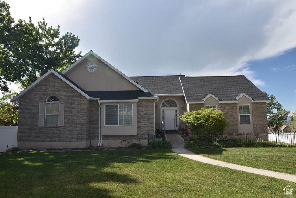 Ranch-style house featuring brick siding, fence, a shingled roof, and a front yard