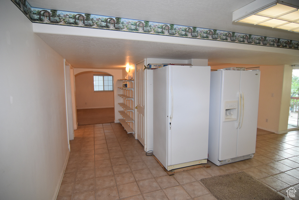 Kitchen featuring white fridge with ice dispenser, freestanding refrigerator, arched walkways, baseboards, and light tile patterned floors