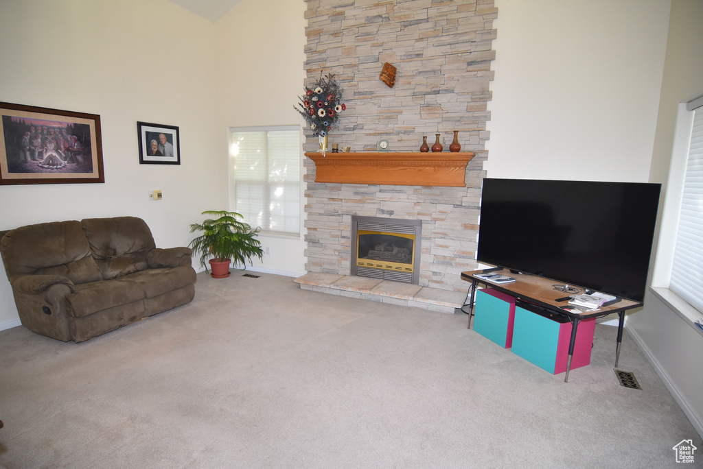Living room featuring carpet, a stone fireplace, baseboards, plenty of natural light, and a towering ceiling