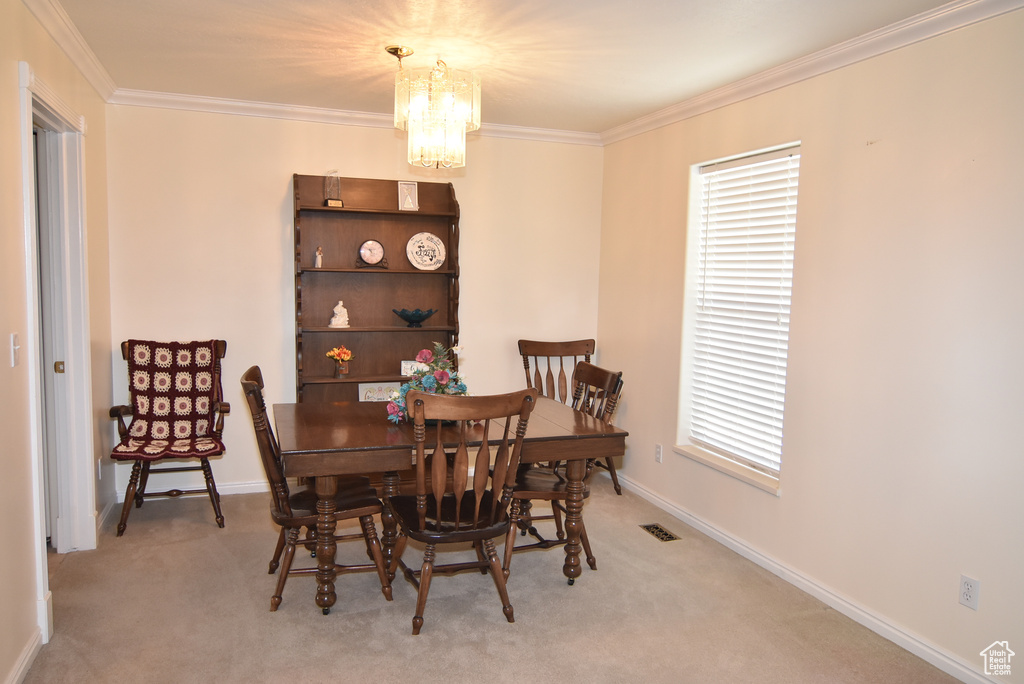 Carpeted dining room featuring a chandelier, ornamental molding, and baseboards