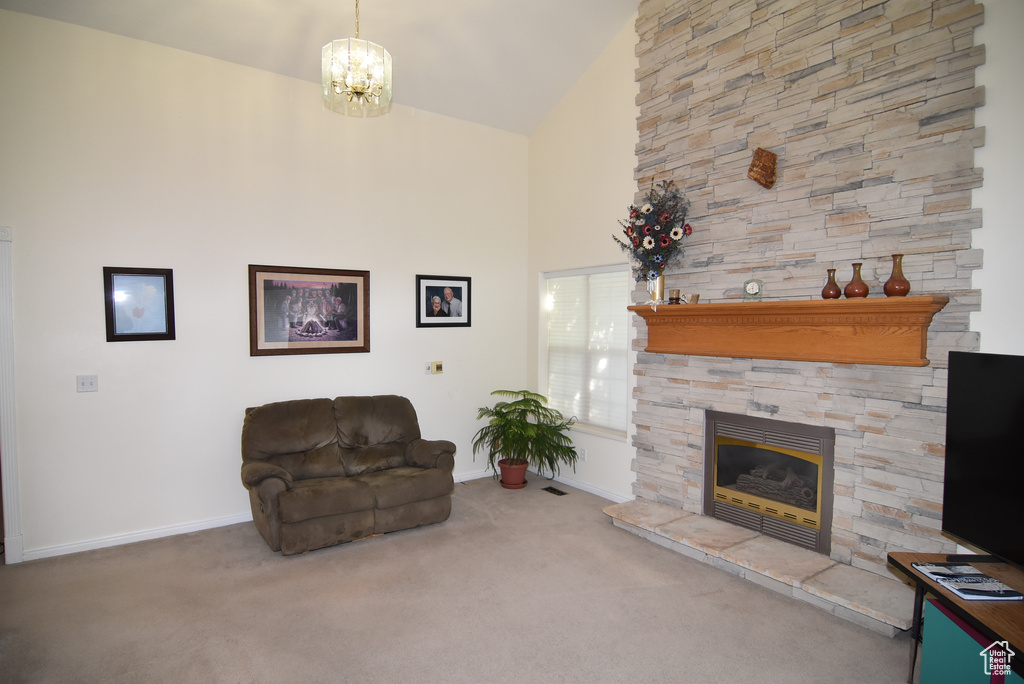 Carpeted living room featuring baseboards, a stone fireplace, high vaulted ceiling, and a chandelier