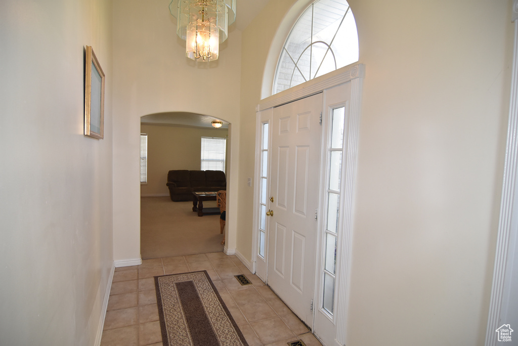 Foyer featuring arched walkways, light tile patterned floors, a towering ceiling, baseboards, and a chandelier