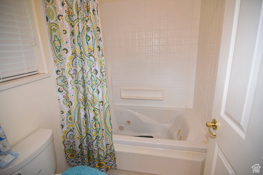 Bathroom featuring a combined bath / shower with jetted tub and toilet