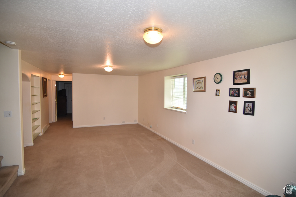 Unfurnished room featuring a textured ceiling, light carpet, baseboards, a smoke detector, and built in features