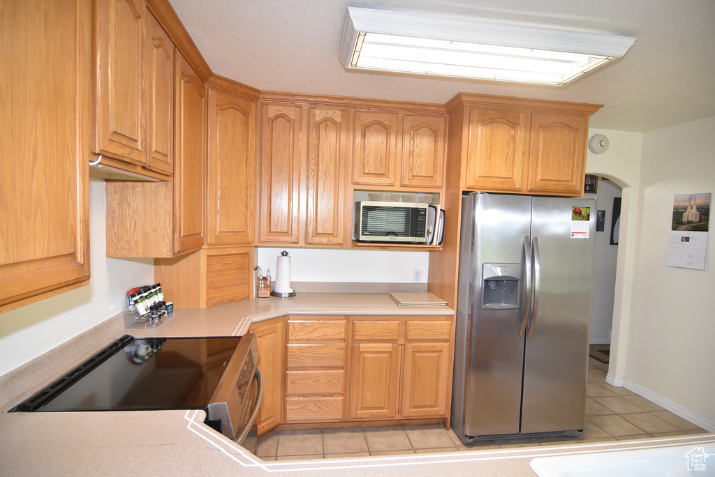 Kitchen featuring appliances with stainless steel finishes, light tile patterned flooring, light countertops, and arched walkways