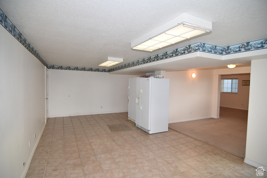Basement featuring white fridge with ice dispenser, a textured ceiling, baseboards, and light flooring