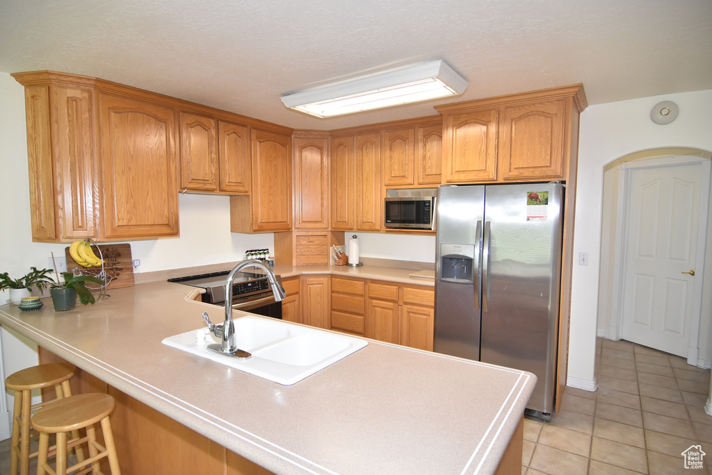 Kitchen with stainless steel appliances, a peninsula, light tile patterned floors, a breakfast bar area, and light countertops
