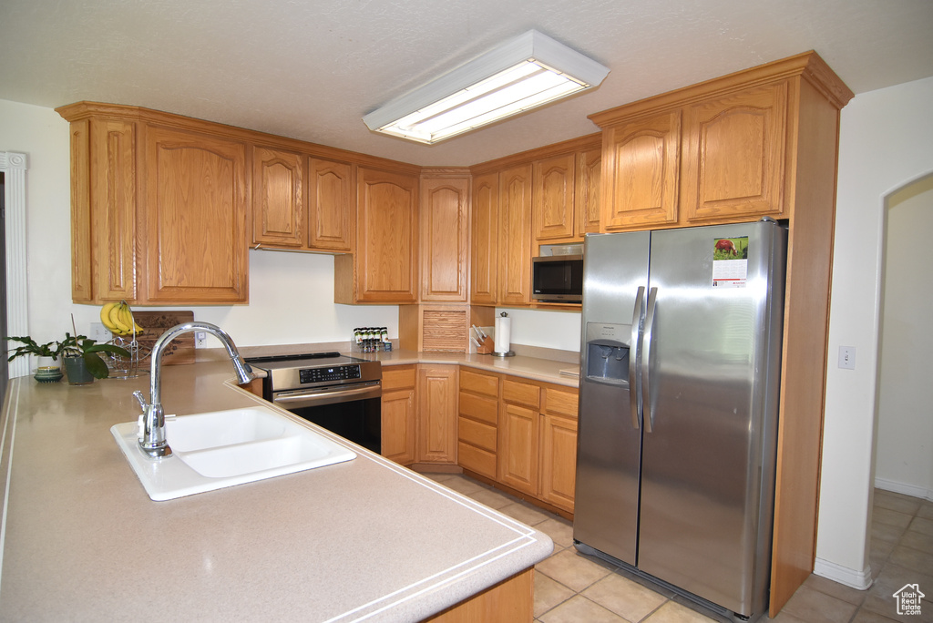 Kitchen with stainless steel appliances, a sink, light tile patterned floors, and light countertops