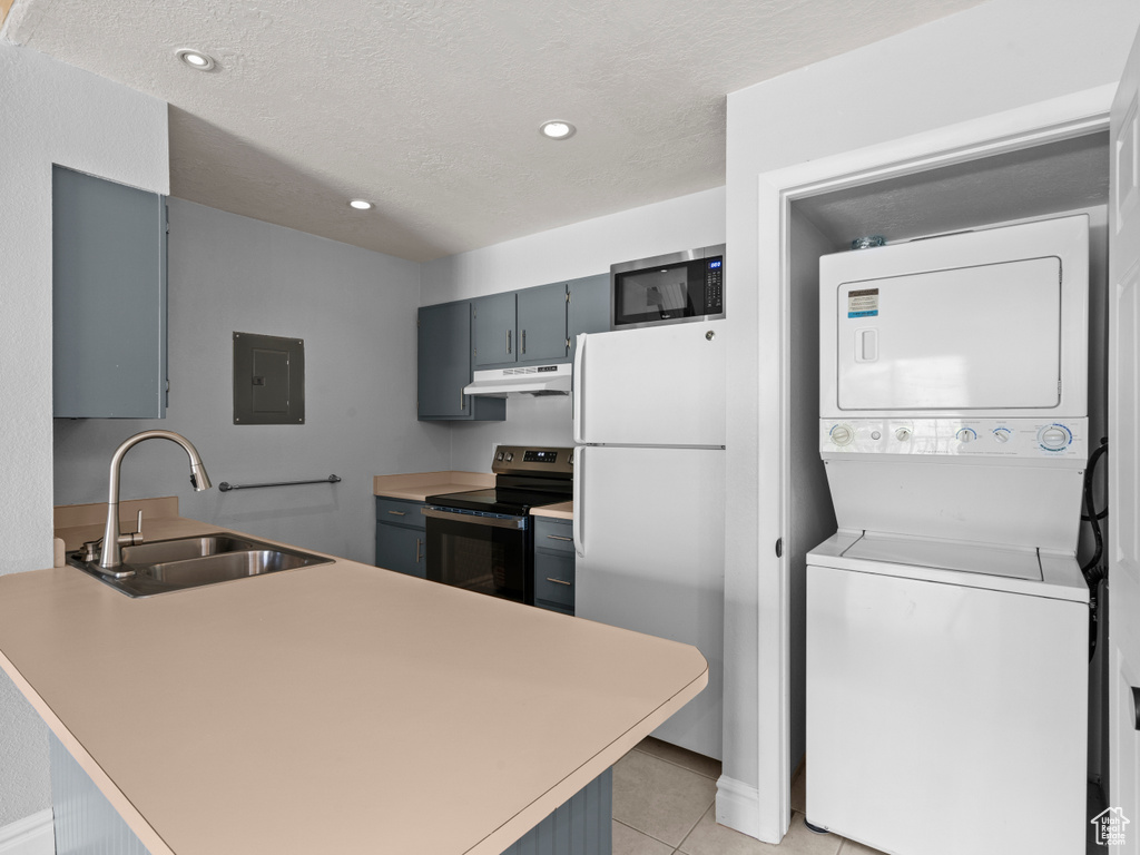 Kitchen with stacked washer / dryer, appliances with stainless steel finishes, a sink, a peninsula, and under cabinet range hood
