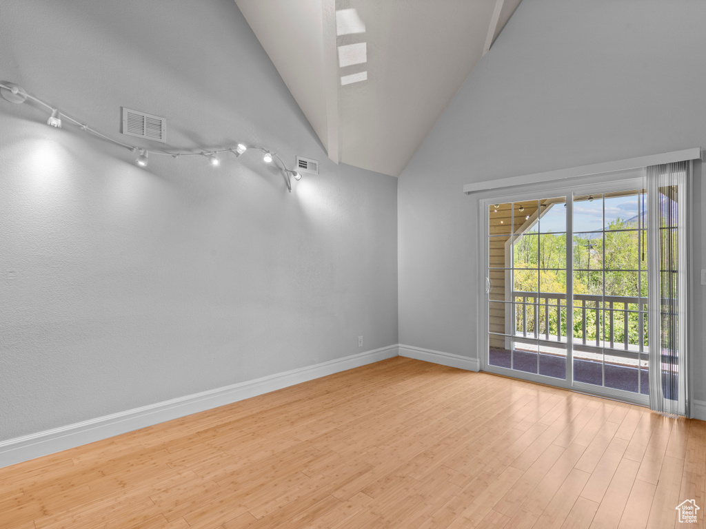 Unfurnished room with baseboards, visible vents, wood finished floors, and high vaulted ceiling