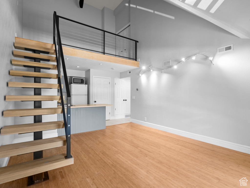 Stairway featuring visible vents, baseboards, wood finished floors, and high vaulted ceiling