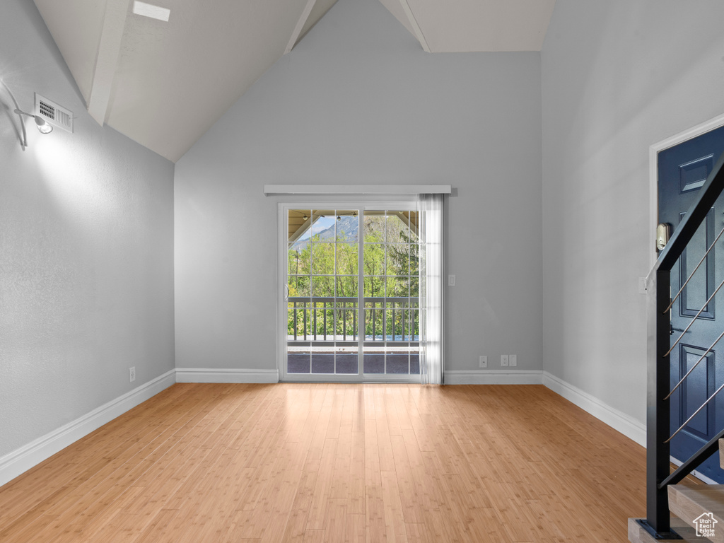 Unfurnished living room with baseboards, visible vents, wood finished floors, and high vaulted ceiling