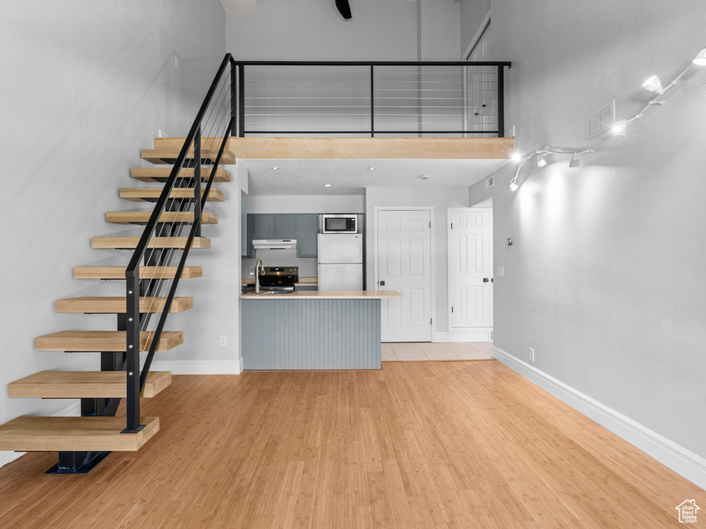 Unfurnished living room with a towering ceiling, visible vents, light wood-type flooring, baseboards, and stairs
