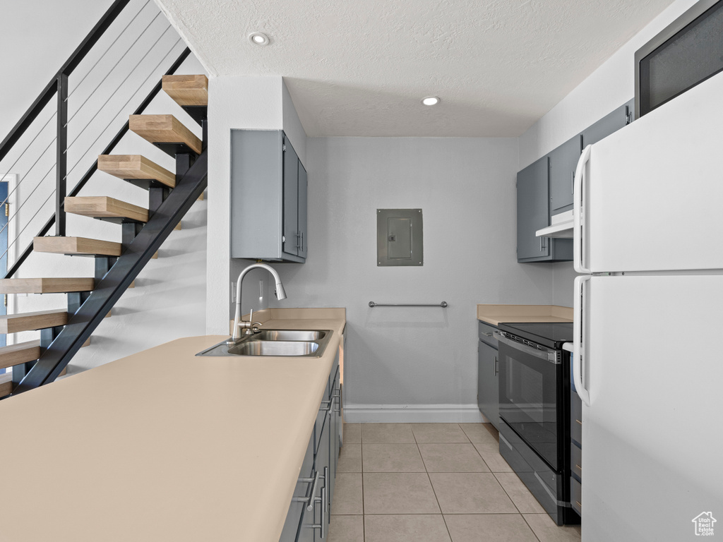 Kitchen with freestanding refrigerator, electric stove, gray cabinets, electric panel, and a sink