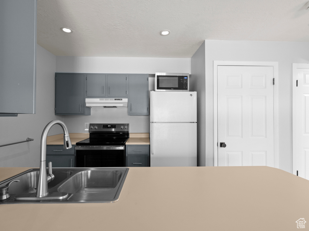 Kitchen featuring a sink, freestanding refrigerator, stainless steel microwave, black range with electric cooktop, and under cabinet range hood