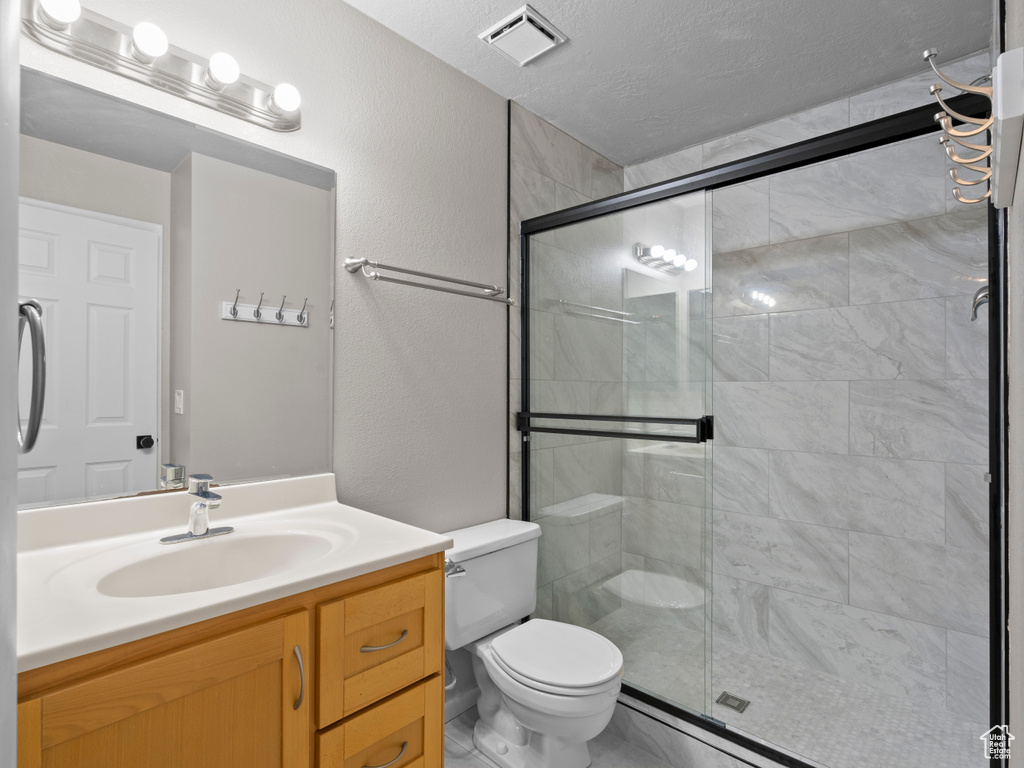 Bathroom with vanity, toilet, a textured ceiling, a shower stall, and visible vents