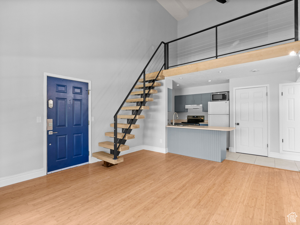 Foyer entrance with a high ceiling, stairs, and light wood-style flooring