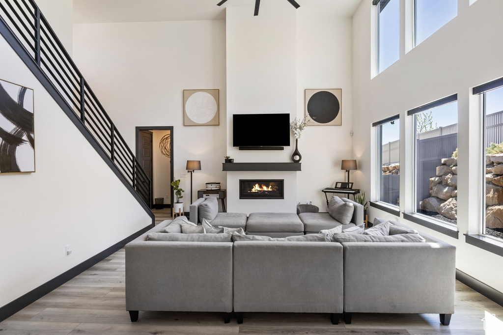 Living area with light wood finished floors, a warm lit fireplace, stairs, and a towering ceiling