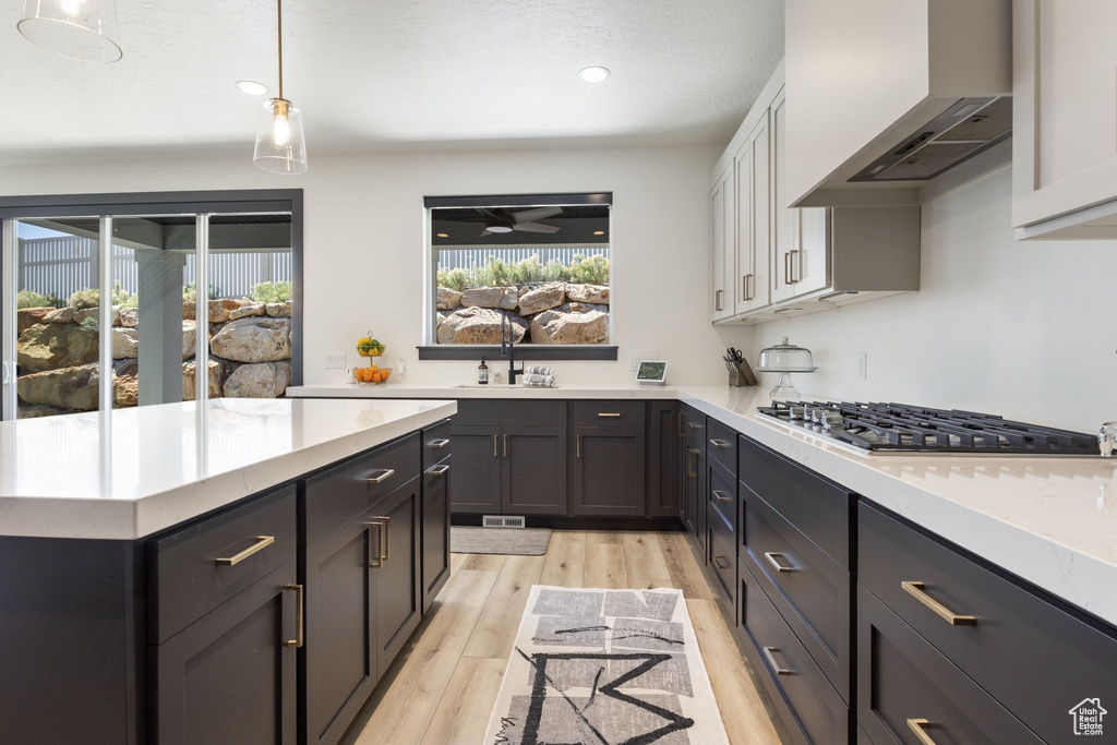 Kitchen featuring light countertops, custom exhaust hood, stainless steel gas stovetop, and a wealth of natural light