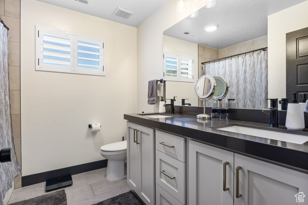 Bathroom with double vanity, toilet, tile patterned floors, and a sink