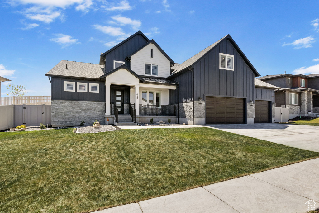 Modern farmhouse style home featuring a gate, board and batten siding, a front lawn, and stone siding