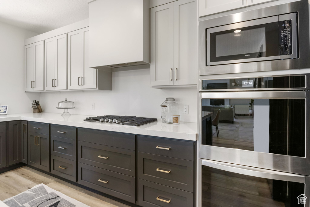 Kitchen featuring appliances with stainless steel finishes, light wood finished floors, light countertops, gray cabinets, and white cabinetry