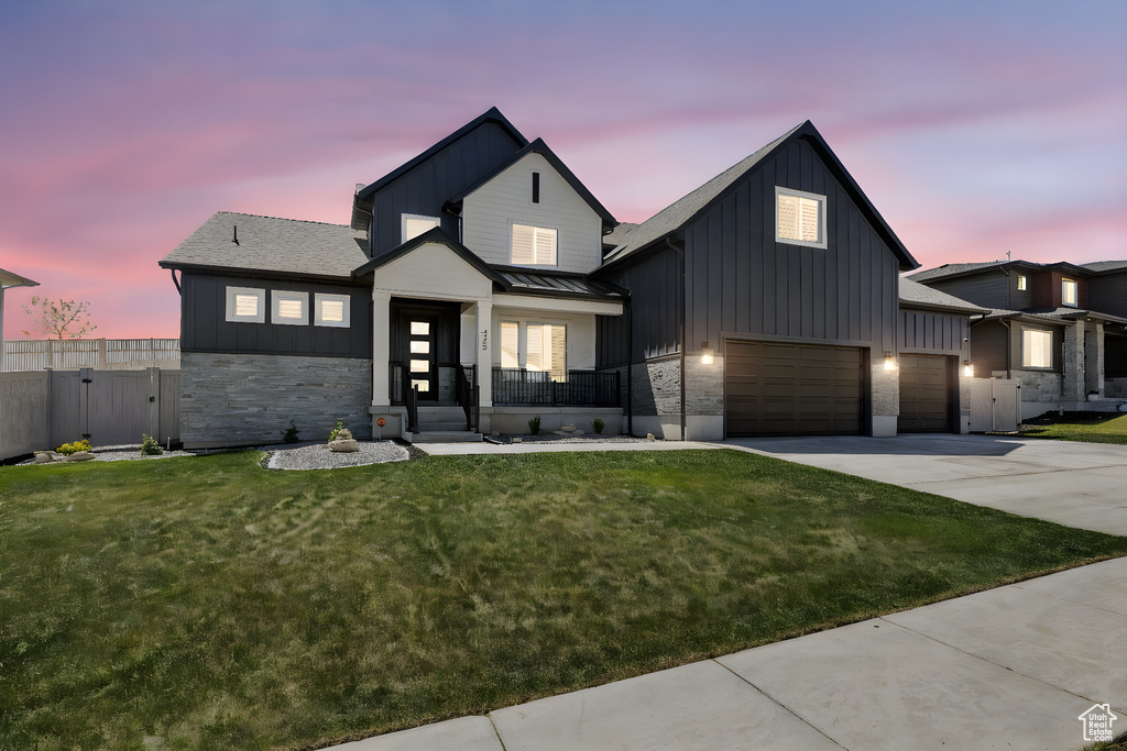 Modern farmhouse featuring a lawn, board and batten siding, driveway, and fence