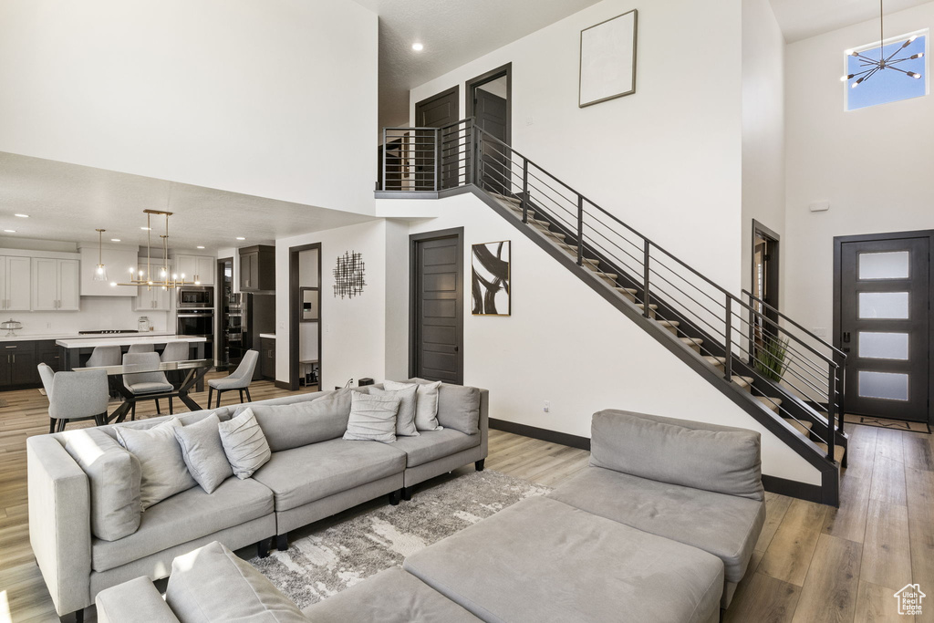 Living area featuring a high ceiling, light wood-style floors, a chandelier, stairs, and baseboards