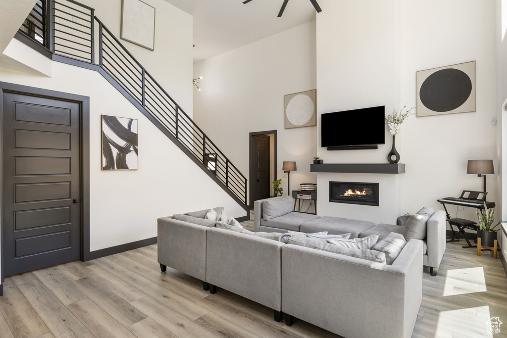 Living area featuring stairs, a glass covered fireplace, baseboards, a high ceiling, and light wood-type flooring