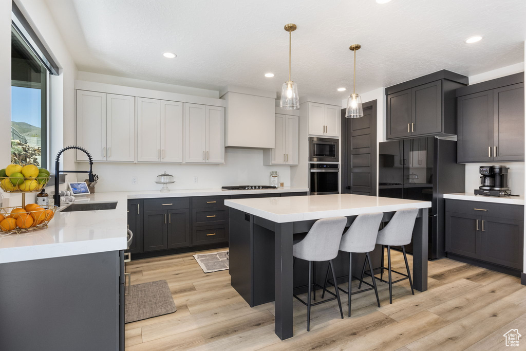 Kitchen featuring a kitchen island, a kitchen bar, a sink, light countertops, and black appliances