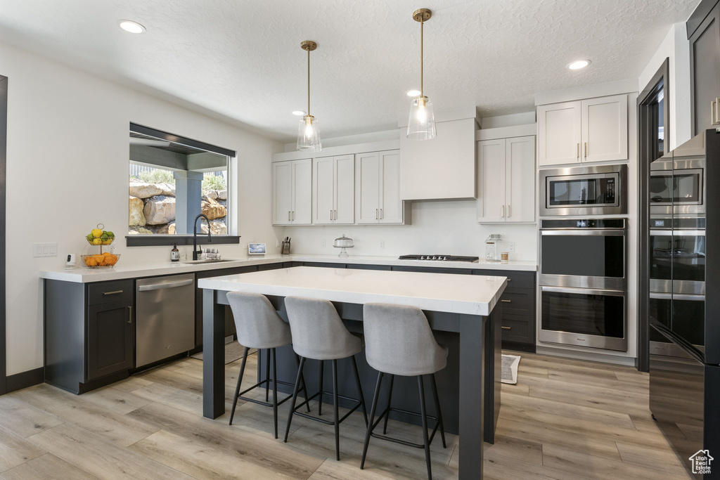 Kitchen featuring a kitchen island, a breakfast bar, light countertops, a sink, and appliances with stainless steel finishes