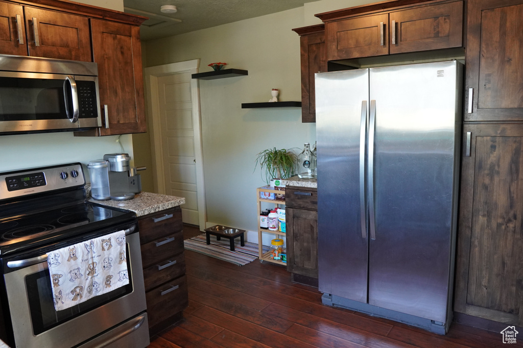 Kitchen featuring light countertops, open shelves, appliances with stainless steel finishes, and dark wood-style floors