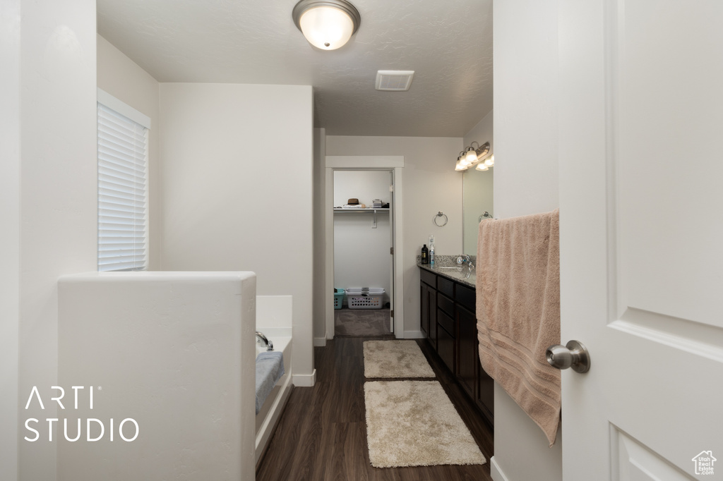 Bathroom featuring vanity, a bath, wood finished floors, and baseboards