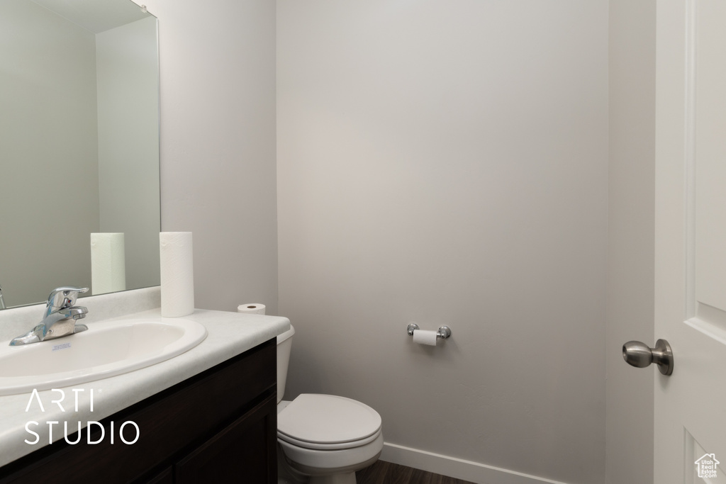 Bathroom featuring vanity, toilet, wood finished floors, and baseboards