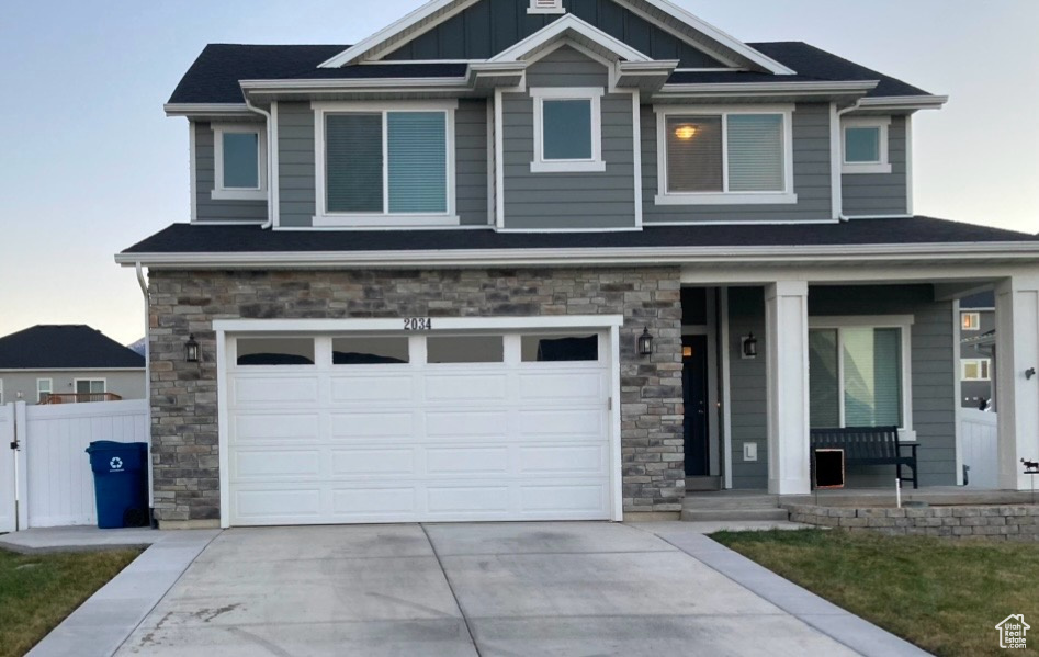 View of front of home with fence, a garage, concrete driveway, stone siding, and a porch