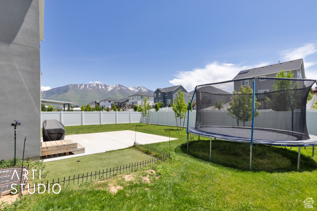 View of yard featuring a trampoline, a patio area, a residential view, and a mountain view