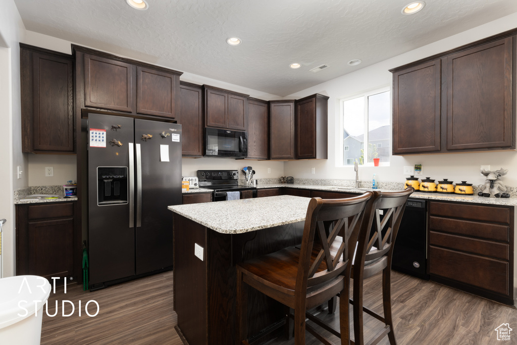Kitchen with black appliances, dark wood finished floors, dark brown cabinets, a center island, and recessed lighting