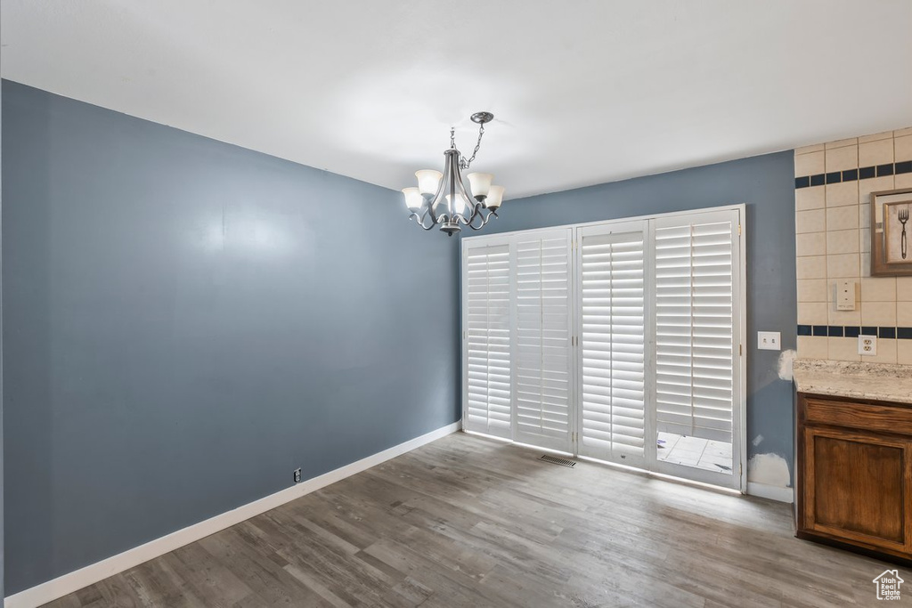 Unfurnished dining area with an inviting chandelier, baseboards, visible vents, and wood finished floors